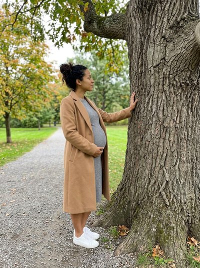 Mulher grávida com a mão numa árvore grande de um parque